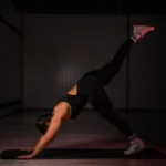 Weronika Tarkowska wykonująca ćwiczenie jogi na macie, unosząc jedną nogę do góry w pozycji psa z uniesioną nogą